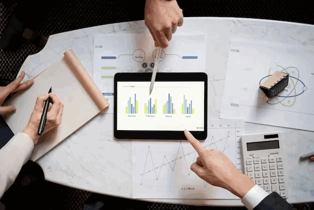 tablet with reporting graphs showing and three people's hands surrounding it